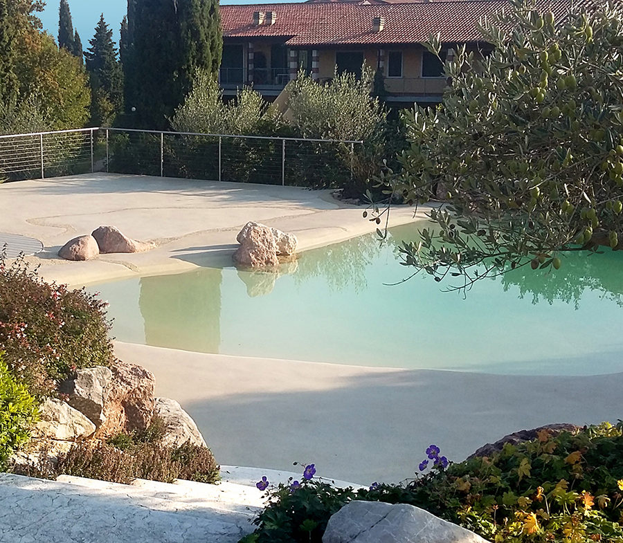 piscine naturelle avec grande plage près d'une maison ancienne dans un jardin paysager
