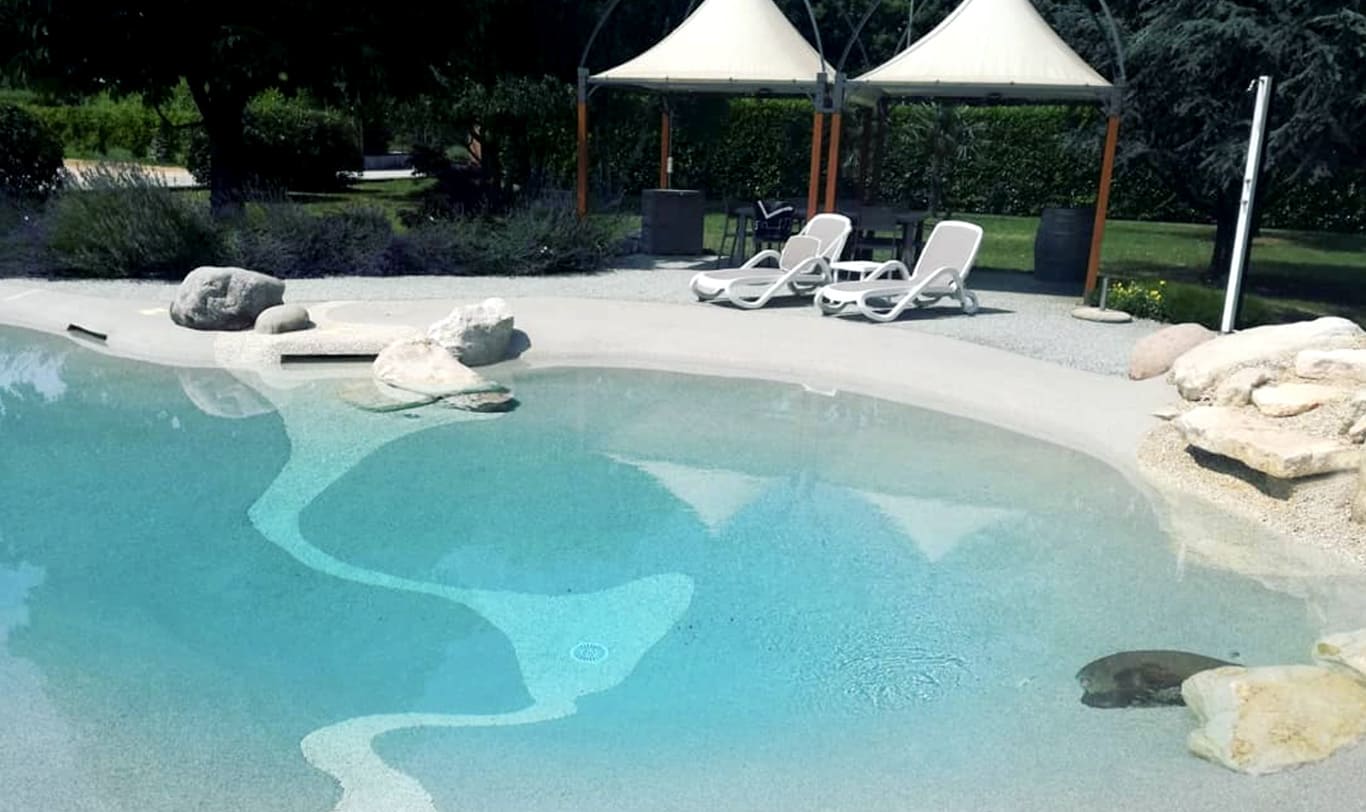 piscine naturelle avec plage, transats et parasols dans un jardin paysagé
